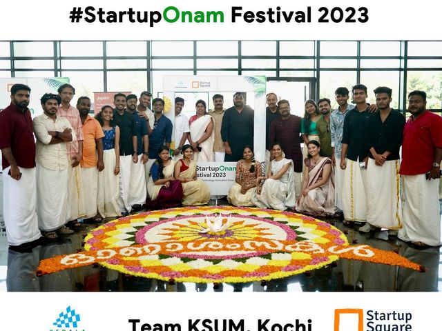 Team KSUM Kochi behind a large circular pookalam at the StartupOnam Festival